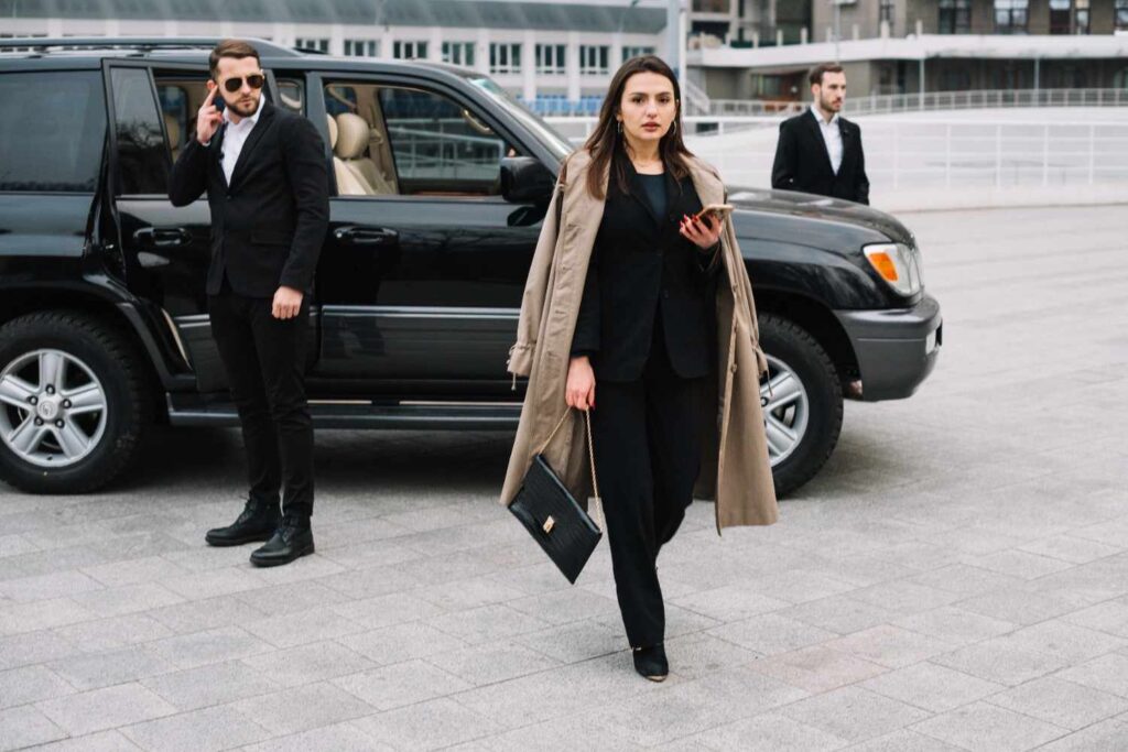 Businesswoman in a suit confidently walking alongside a luxury car, representing professional Chauffeur Service Dubai.