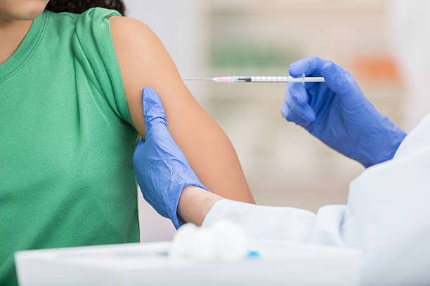 Healthcare professional wearing blue gloves administering a vaccine injection to a patient’s upper arm in a clinical setting.