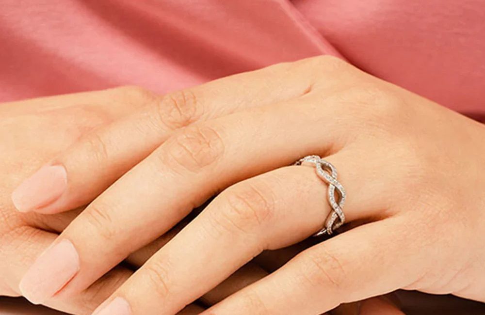 Woman wearing an infinity twist diamond ring with a delicate intertwined design on her finger.